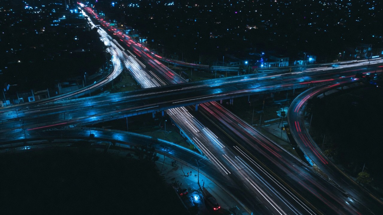 Vista aérea nocturna de un entronque vial de la Ciudad de México con estelas de luz de los vehículos en larga exposición